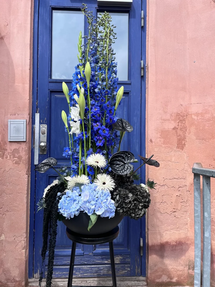 Høj dekoration med blå hortensia, ridderspore og hvide blomster ved en blå dør