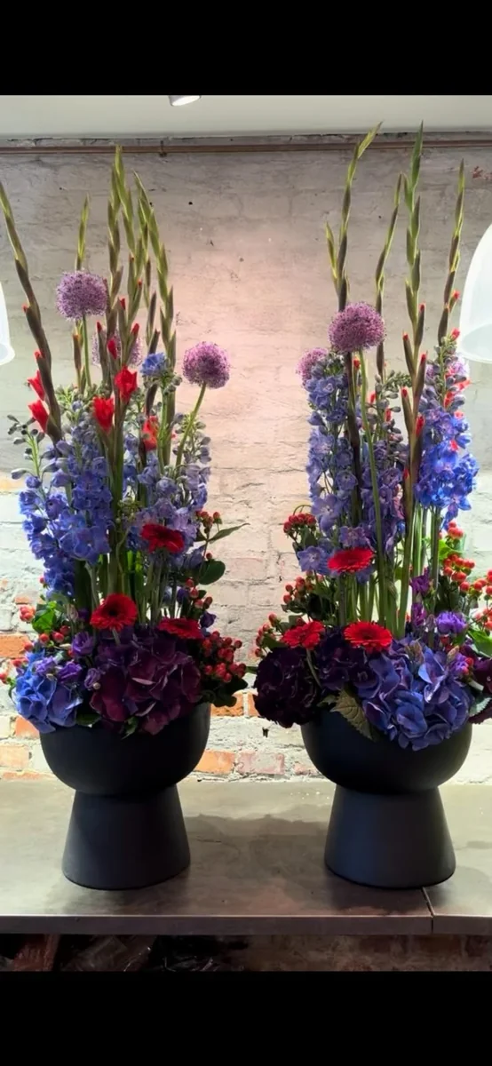 To høje arrangementer med røde roser, blå ridderspore og lilla blomster