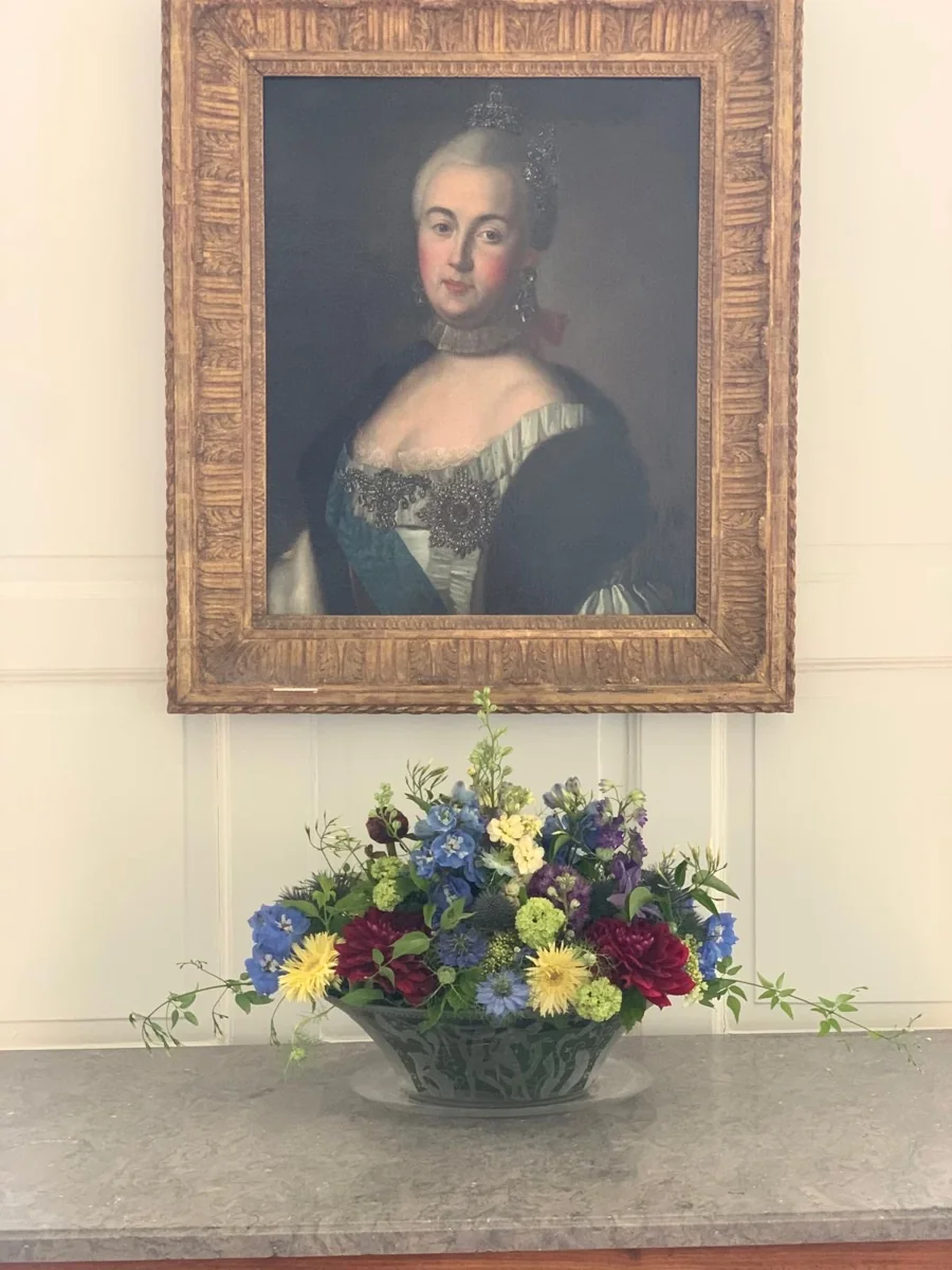 Skåldekoration med blå, gule og hvide blomster under et indrammet portræt
